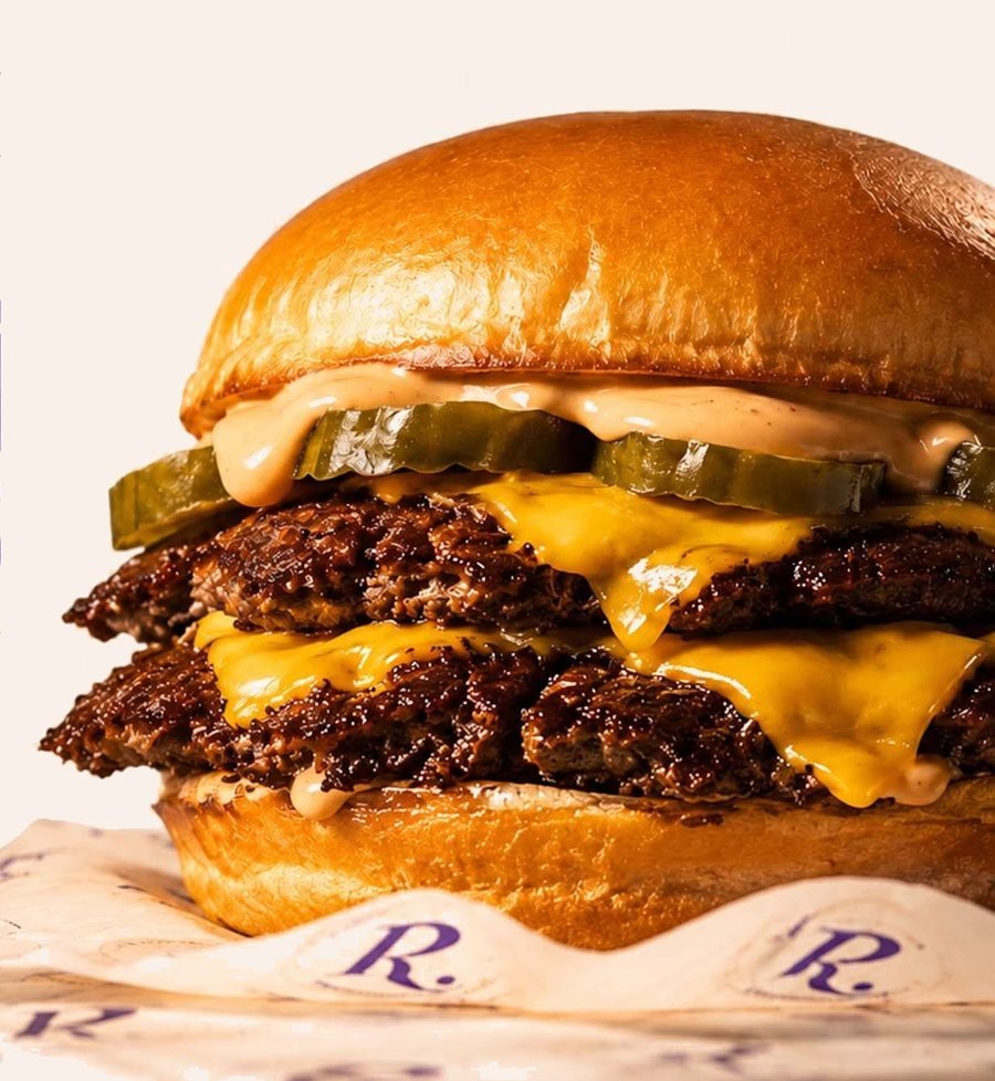 Doble smash burger con cheddar fundido, pepinillos y Ruggier Sauce sobre papel encerado con la R. de Ruggier